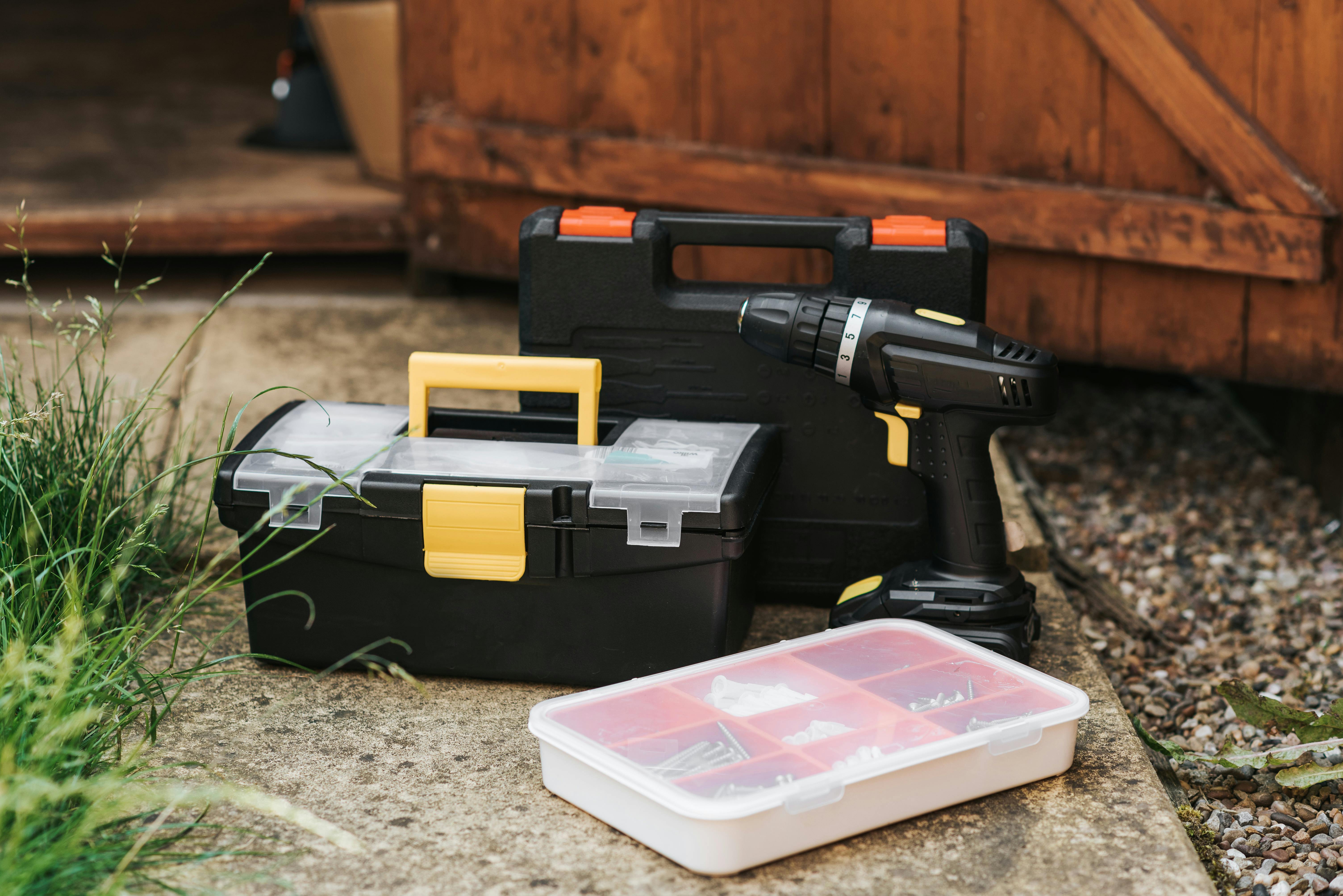 Toolboxes and power drill on a concrete surface near a garage
